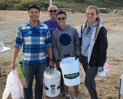Smiling group of people at the beach cleanup with gloves, buckets, and trash bags