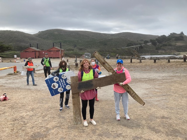 People carrying large planks of wood and other large trash at the beach cleanup.