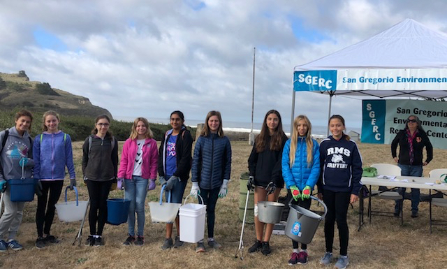 Group of beach cleanup volunteers holding buckets of trash, standing in front of the SGERC registration tent.