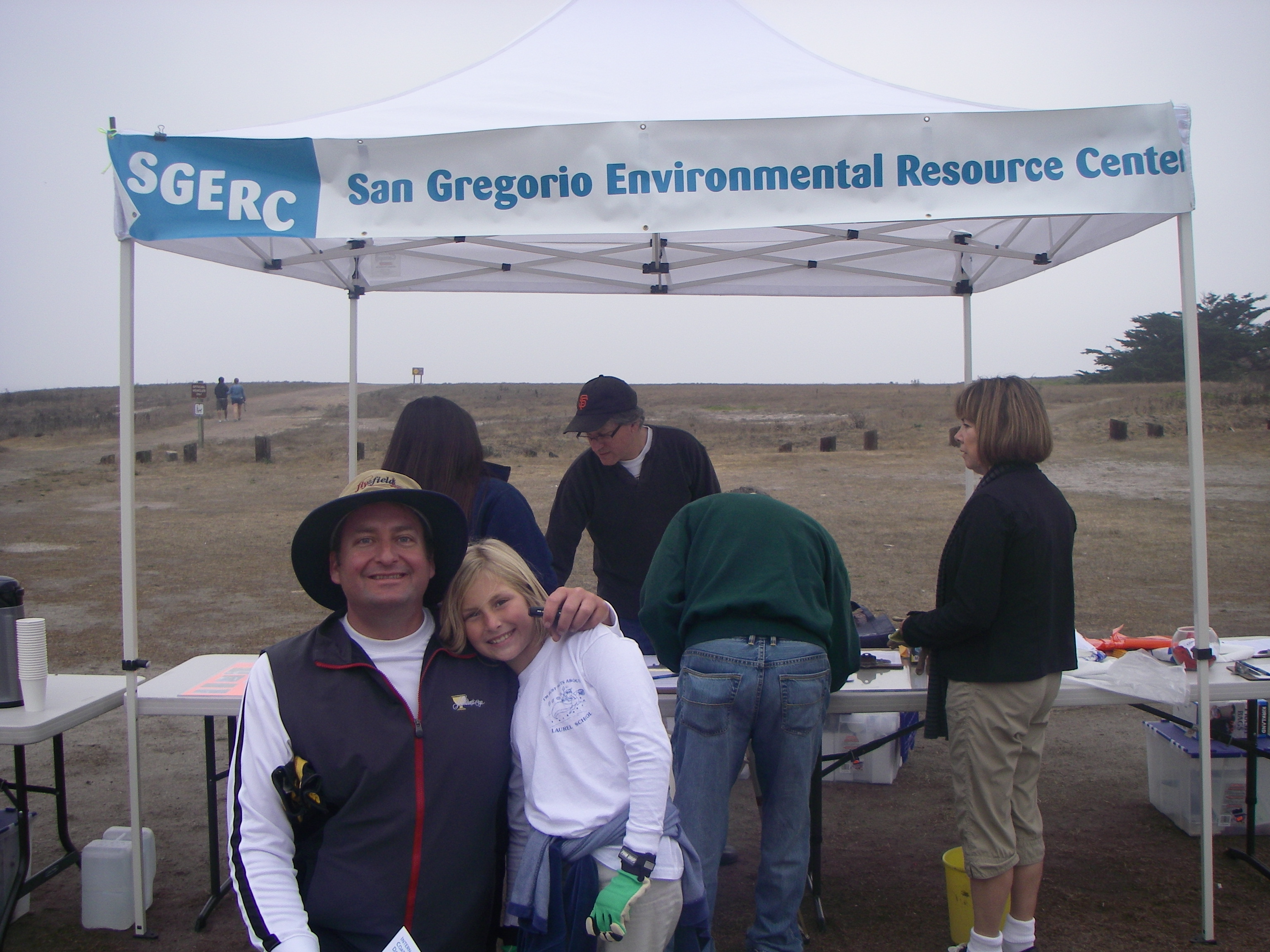 Parent and child smiling in front of the SGERC tent at a beach cleanup.