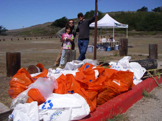 A family smiles while standing behind a large pile of bags containing trash collected during a beach cleanup at San Gregorio State Beach.